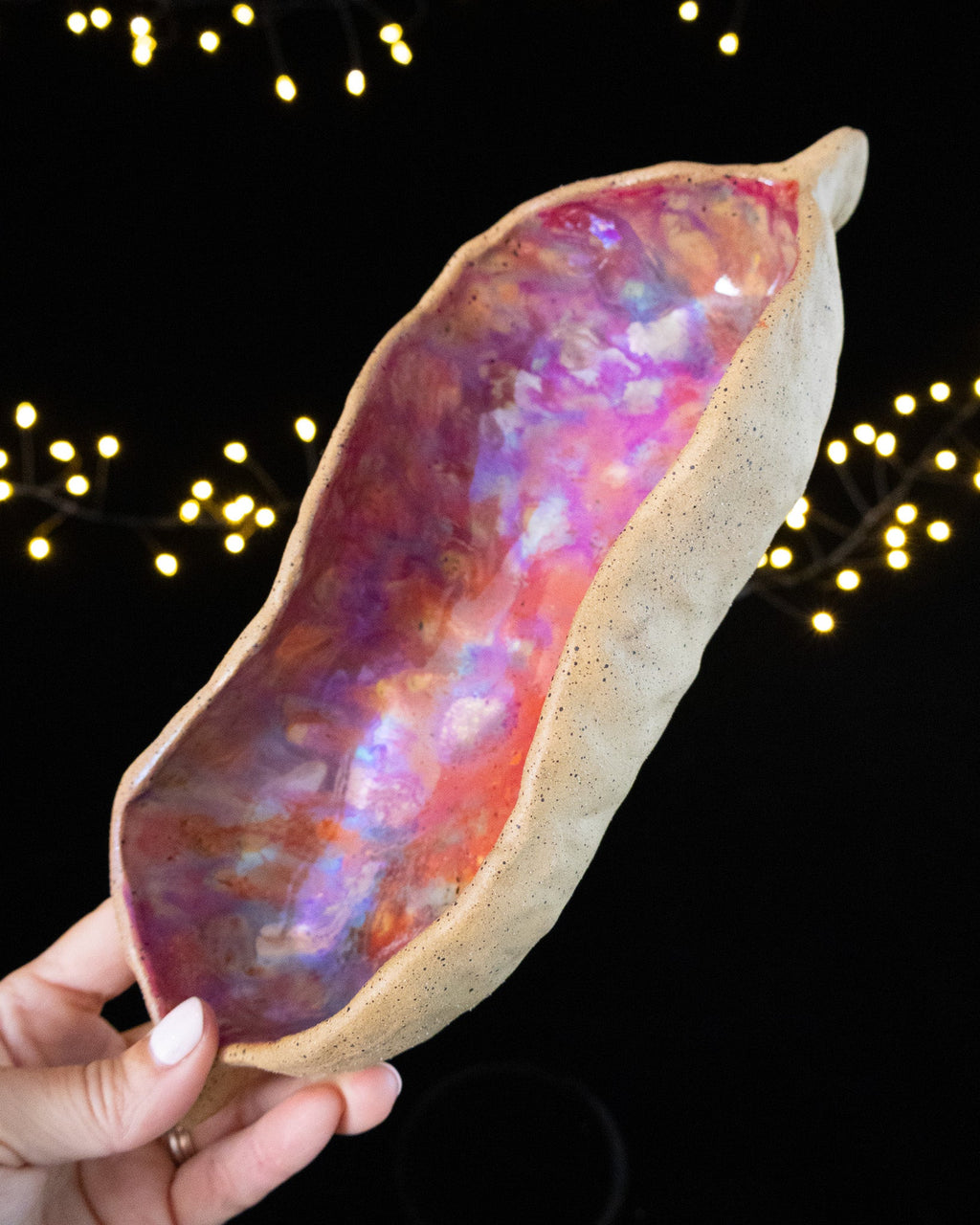 Bare speckled stoneware outside, iridescent pink luster within the pod