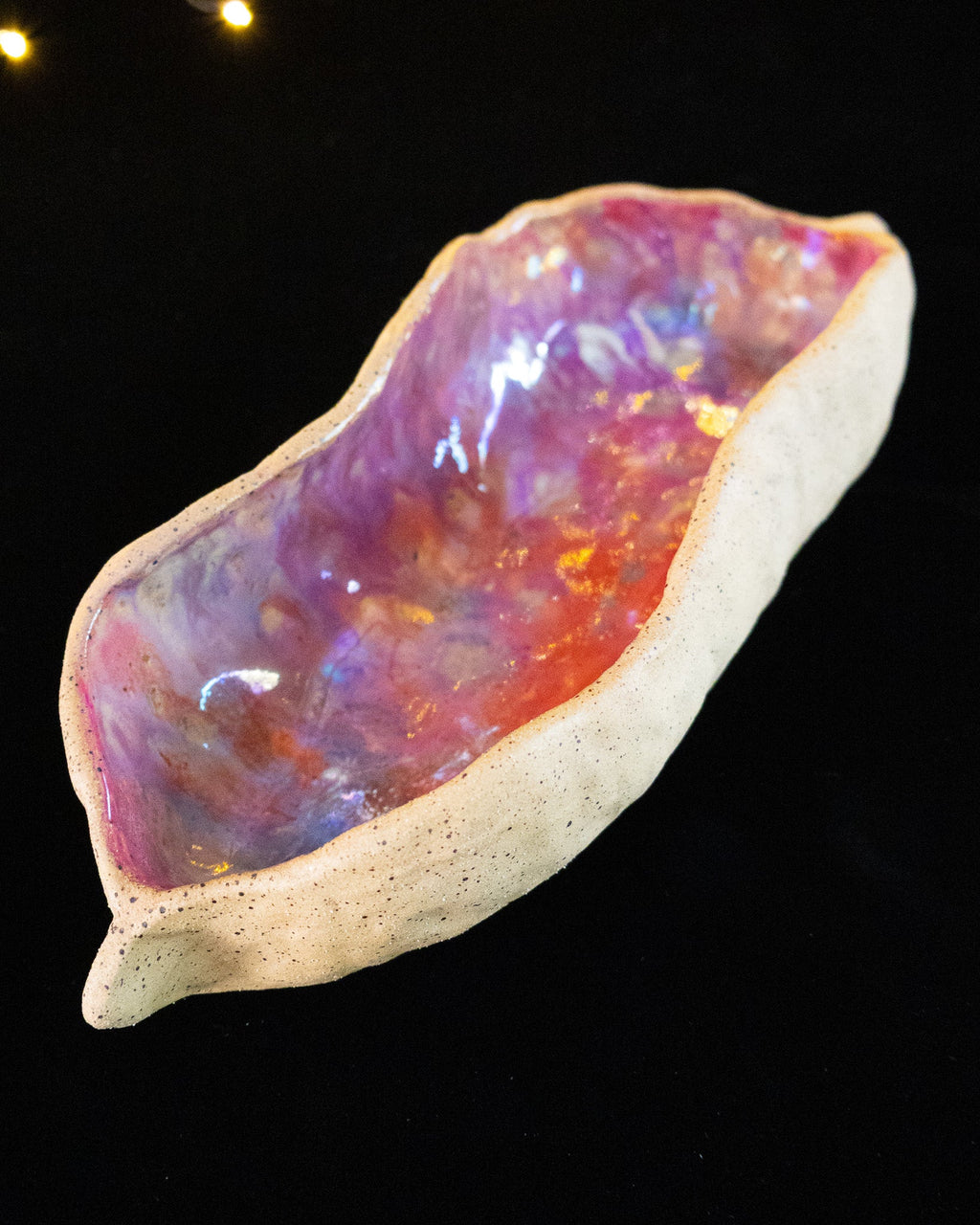 Handmade ceramic seed pod held in hand against fairy lights