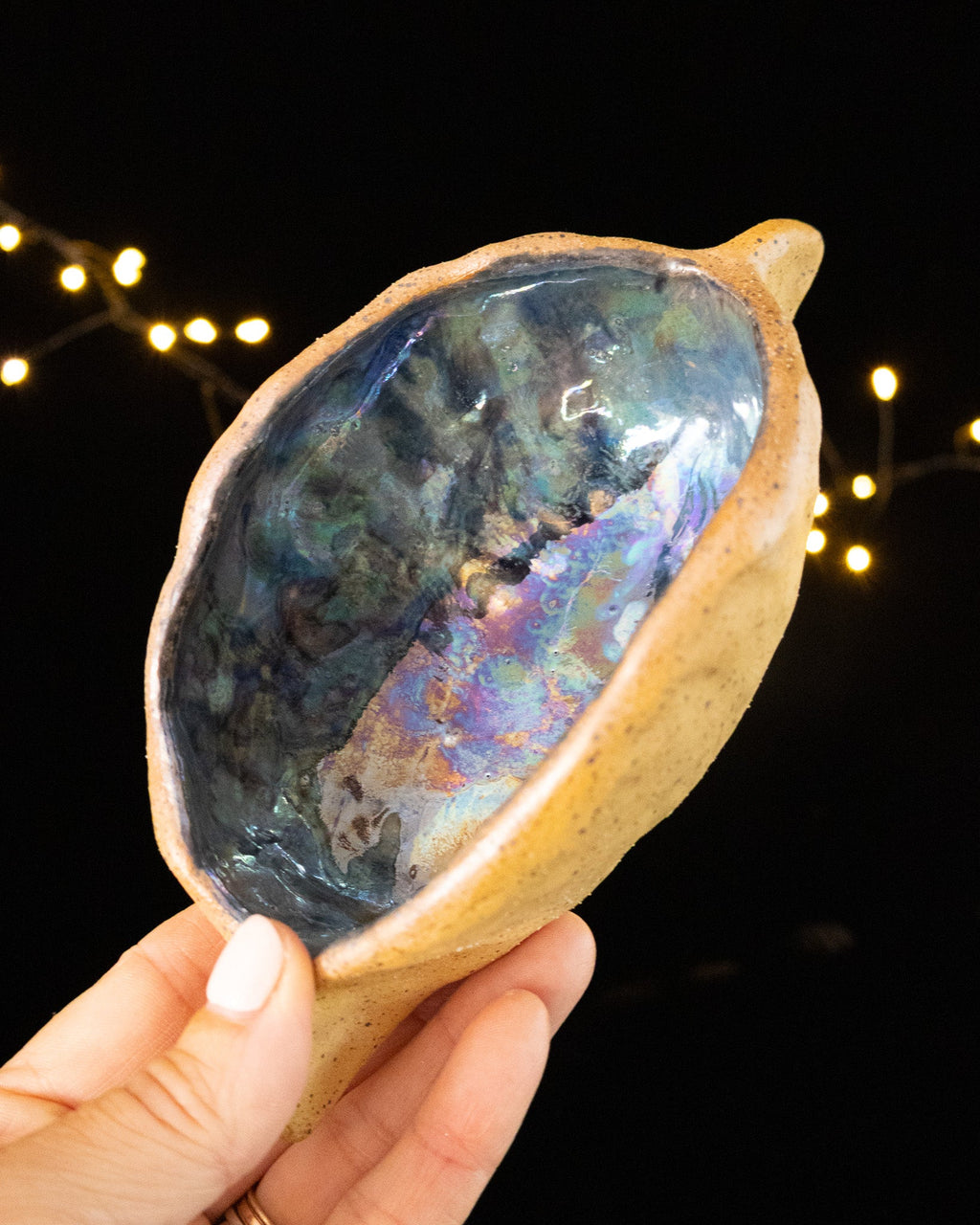 Bare speckled stoneware outside, deep blue iridescence within the pod