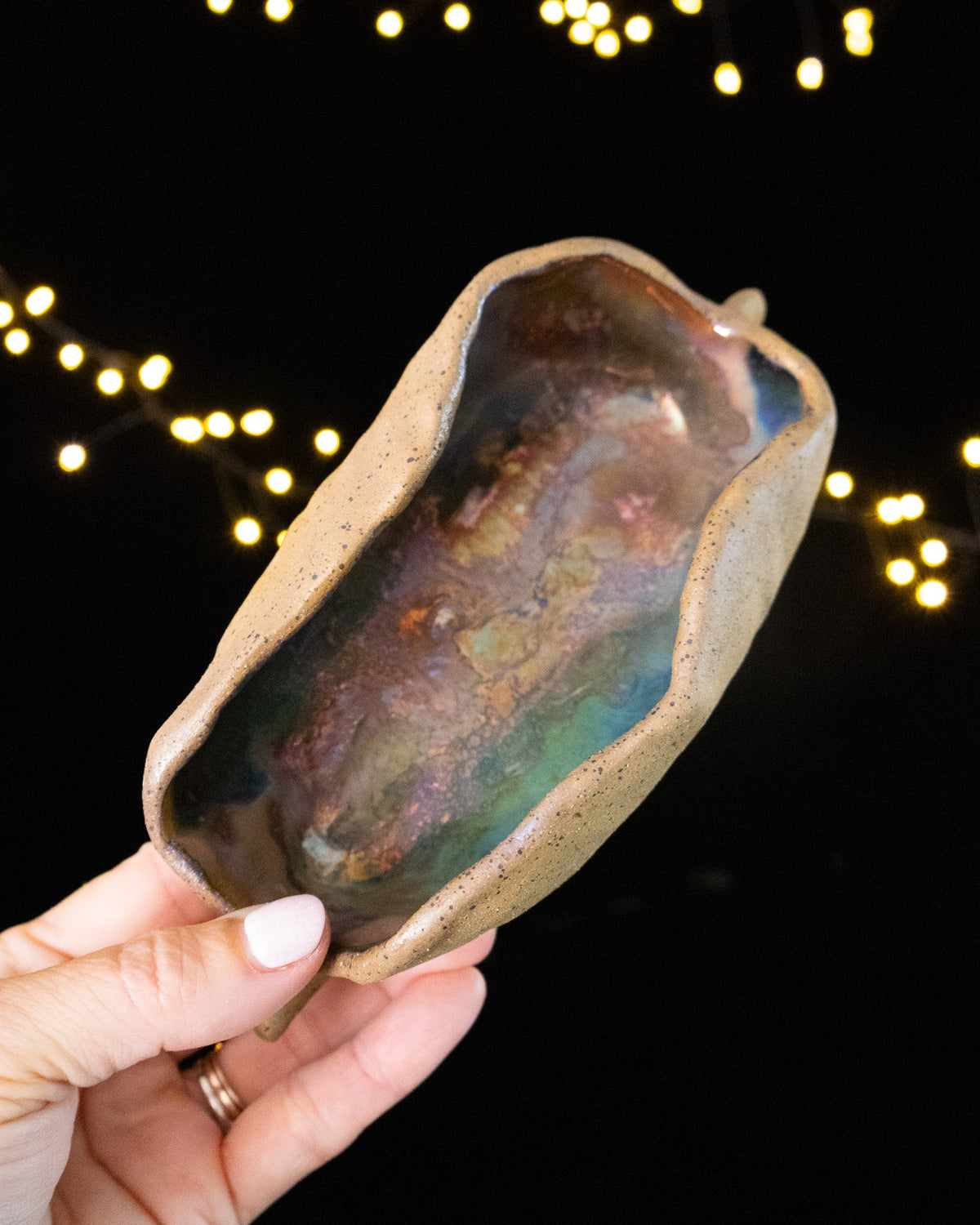 Bare speckled stoneware outside, deep teal iridescence within the pod