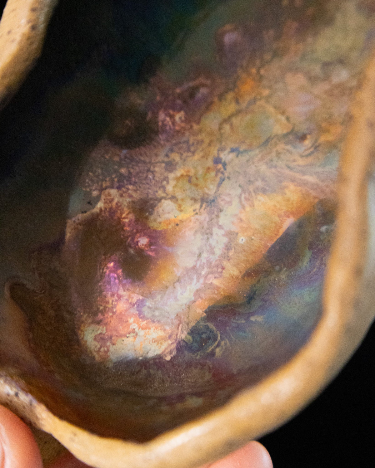 Close detail of teal and warm rust luster inside a ceramic seed pod