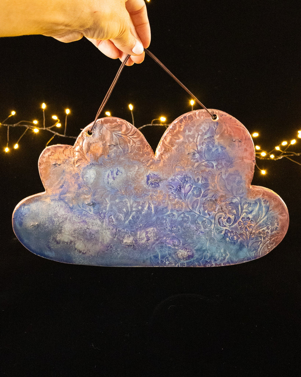 Cloud shaped ceramic jewelry wall display in rose, blue and violet luster, hanging from a leather cord