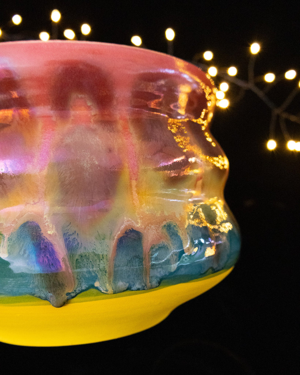 Angled view of a colourful wheel thrown planter with teal drips