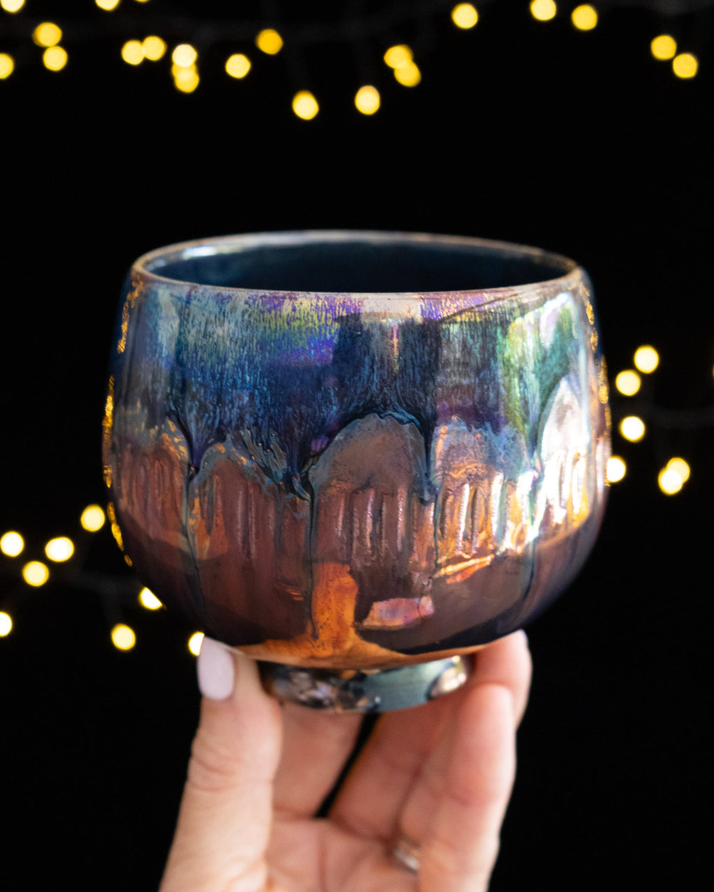 Handmade lusterware ritual cup in deep blue and warm amber, held against fairy lights