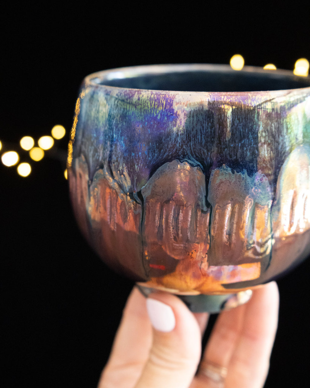 Pale drips running down the body of a handmade iridescent ceramic cup