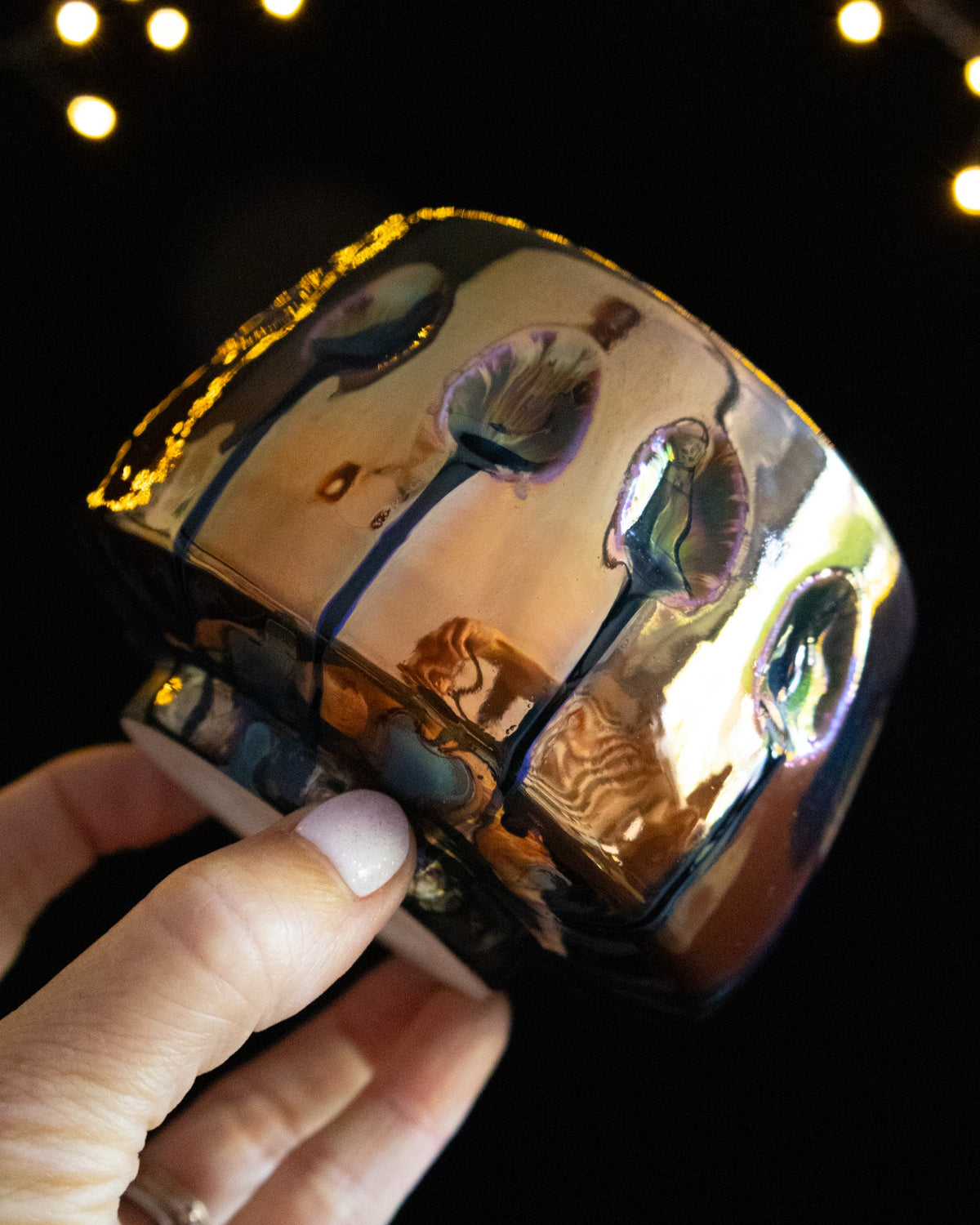Wheel thrown porcelain cup with amber in-glaze luster, held in hand