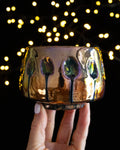 Oval impressions trailing dark lines on an iridescent amber ceramic cup