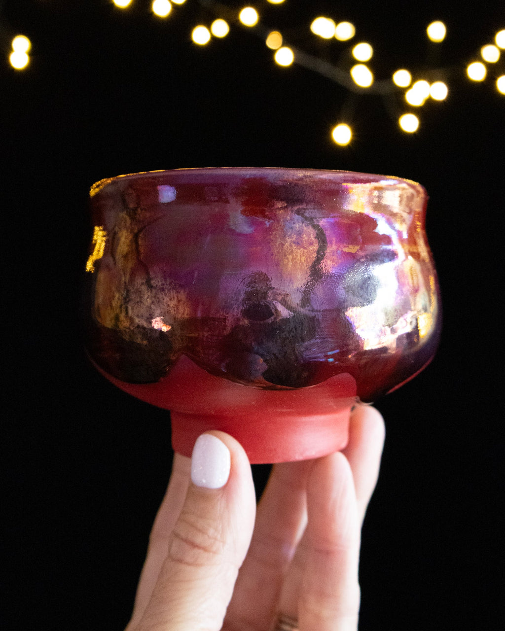 Handmade lusterware ritual cup in garnet red and coral, held against fairy lights